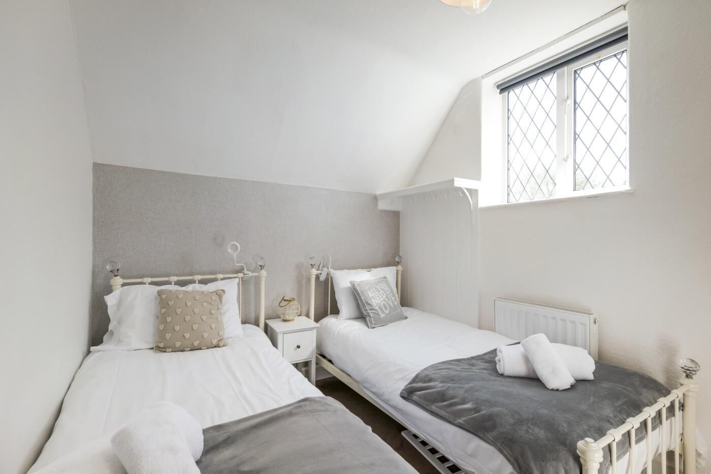 Een slaapkamer met twee bedden, een raam met een rasterpatroon en een radiator.