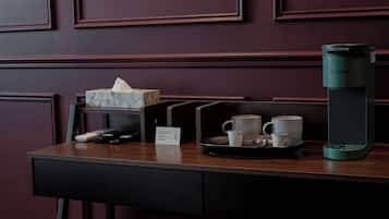 Uma mesa de madeira escura com uma cafeteira Keurig, um suporte com duas chávenas, uma caixa de lenços de papel e um comando à distância.