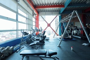 Ett gym med träningsutrustning, ett fönster med utsikt över staden och ett rött, bärande konstruktionselement.