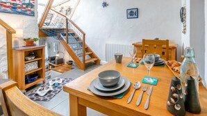Een eetgedeelte met een houten tafel gedekt voor twee personen, een trap met een blauw net, en uitzicht op buiten.