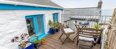 A balcony with a wooden deck, potted plants, a folding chair, and a table with a tray.