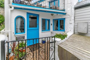 Ein weißes Gebäude mit blauen Akzenten, einem Balkon und einer Holzterrasse.