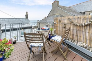 A wooden deck with two chairs and a table, overlooking a body of water. - 1 Bed in Porthleven (oc-smuggl) (Porthleven)
