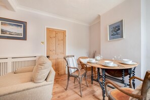 A cozy living room with a beige sofa, a wooden dining table set for four, and a wooden door. - 3 Bed in Cromer (oc-2254) (Cromer)