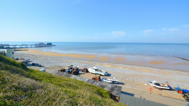 Uma praia costeira com barcos, um cais e uma área gramada.