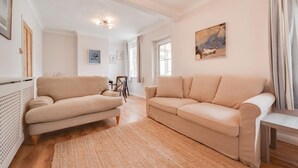 Uma sala de estar com um sofá bege, uma mesa de centro de madeira e um quadro na parede.
