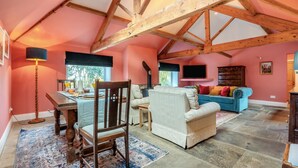 Ein großzügiges Loft mit freiliegenden Holzbalken, einem Essbereich mit Tisch und Stühlen, einer Couch und einem an der Wand befestigten Fernseher.