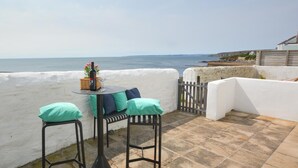 A terrace with a table set for two, a white wall, and a view of the sea. - 2 Bed in Porthleven (oc-marin2) (Porthleven)