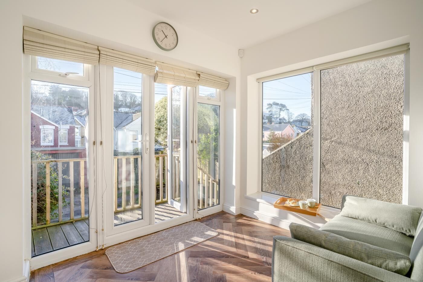A bright room with a large window, a clock, and a green sofa.