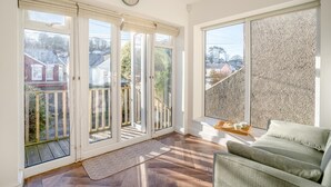 Una habitación luminosa con un ventanal grande, un reloj y un sofá verde.