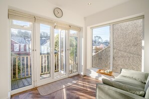 Ein helles Zimmer mit einem großen Fenster, einer Uhr und einem grünen Sofa.