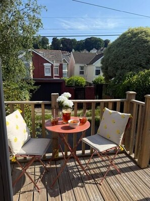 A wooden deck with a small table and two chairs, surrounded by a wooden railing. - 3 Bed in Mumbles (oc-t34004) (The Mumbles)