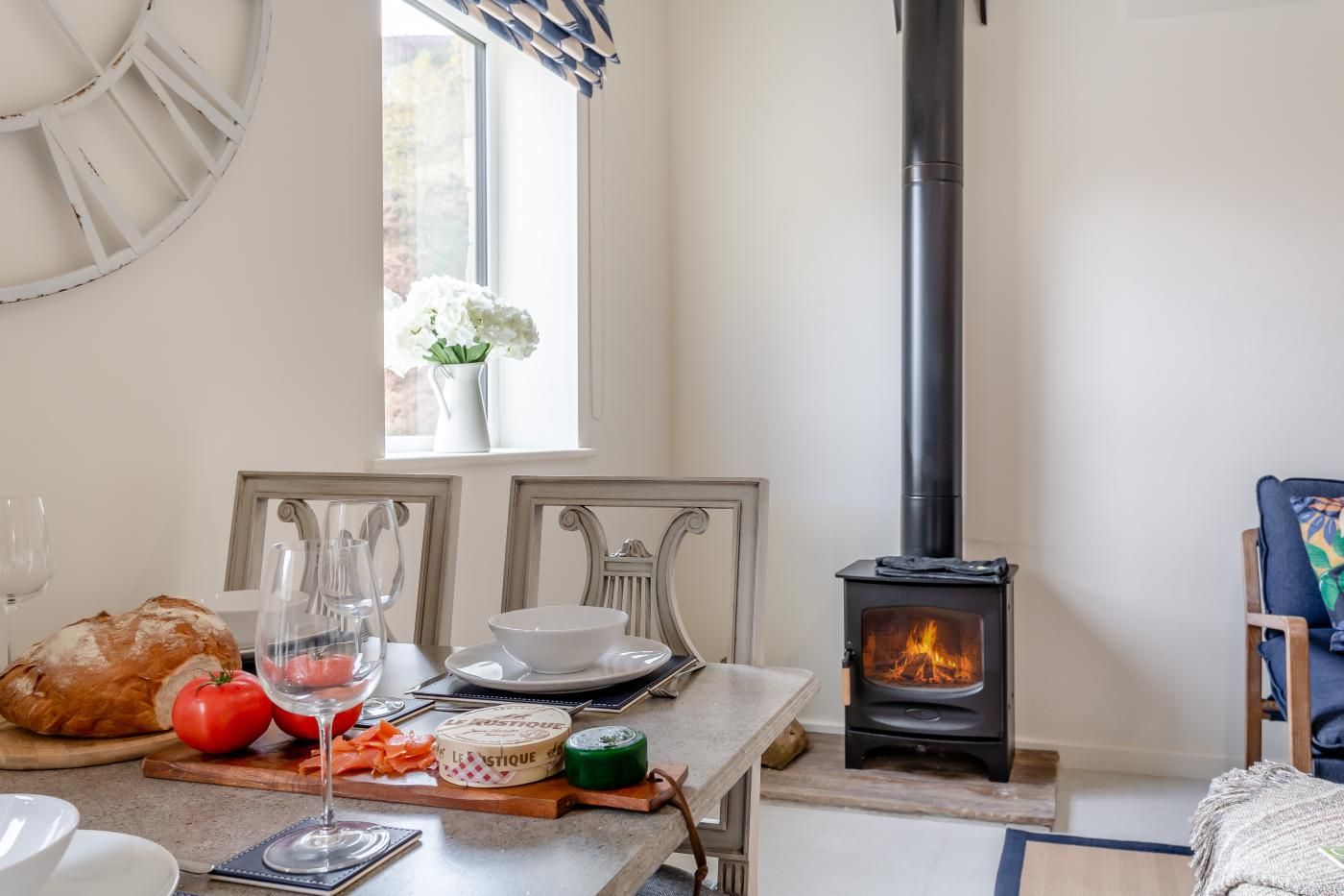 A cozy dining area with a table set for a meal, a wood-burning stove, and a window with curtains.