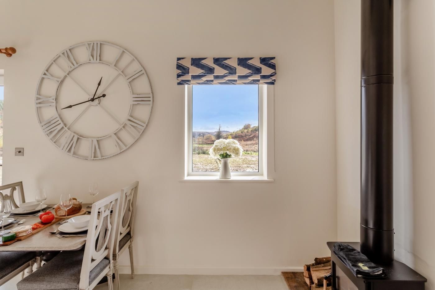 A dining area with a large wall clock, a window with a view of a landscape, and a fireplace.