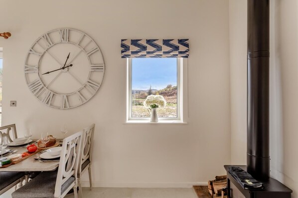 A dining area with a large wall clock, a window with a view of a landscape, and a fireplace.