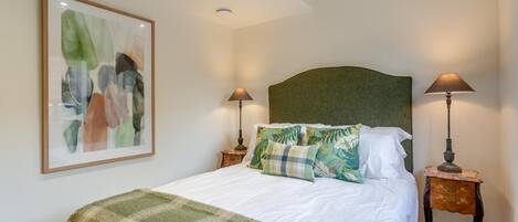 A neatly made bed with a green blanket, two bedside lamps, and a framed abstract painting on the wall.