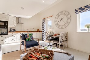 A modern kitchen with white cabinetry, a dining area with a table and chairs, a large wall clock, and a window with a view. - 2 Bed in Dunsop Bridge (oc-w33524) (Dunsop Bridge)