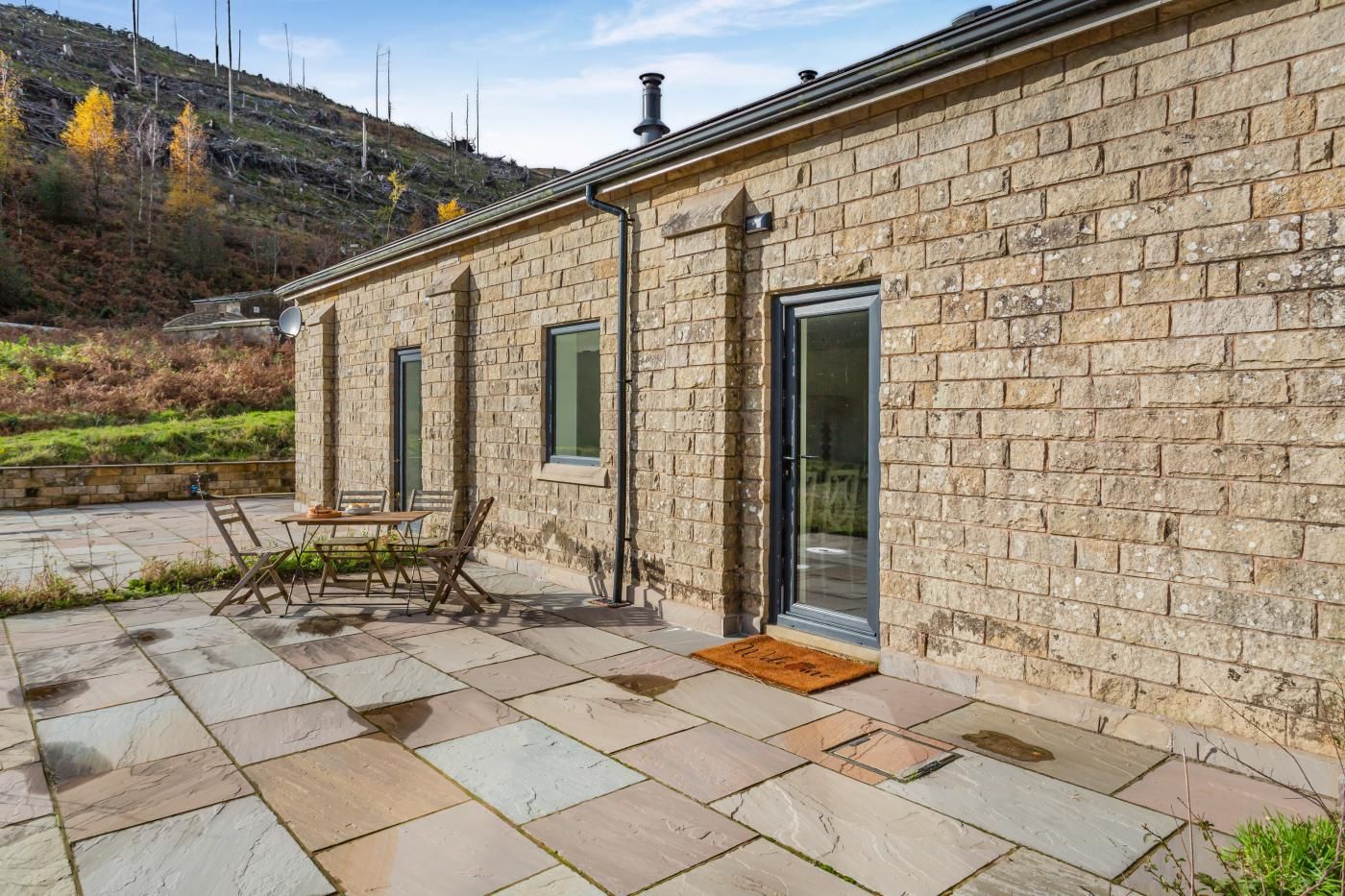 A stone building with a patio area, a table with chairs, and a door with a glass panel.