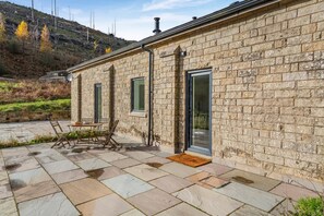 A stone building with a patio area, a table with chairs, and a door with a glass panel.