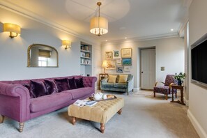 Ein Wohnzimmer mit einem violetten Sofa, einem blauen Sofa, einem Holzstuhl und einem kleinen Tisch mit einem Blumenstrauß.
