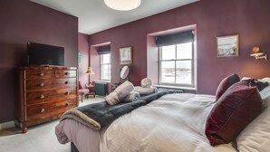 Une chambre à coucher avec un grand lit, une commode, un téléviseur et une fenêtre donnant sur un beau paysage.