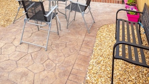 Eine Terrasse mit einem runden Tisch, vier Stühlen, einer Bank und einem Blumentopf.