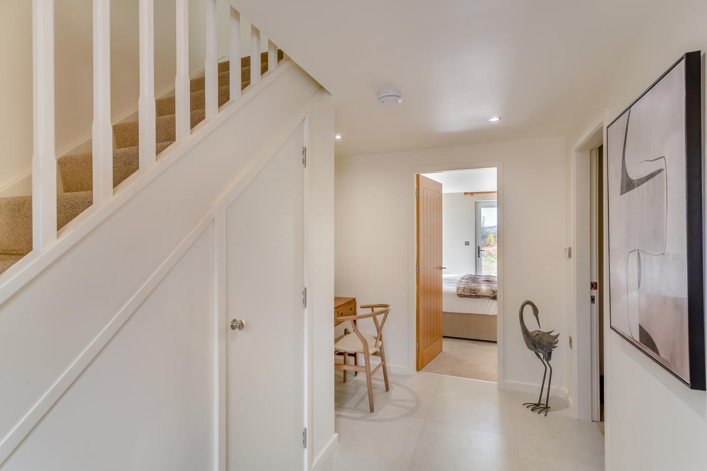 A hallway with a staircase, a dining area with chairs and a table, and a large abstract painting on the wall.