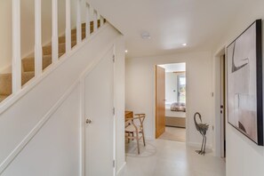 Un couloir avec un escalier, un coin repas avec des chaises et une table, et un grand tableau abstrait accroché au mur.