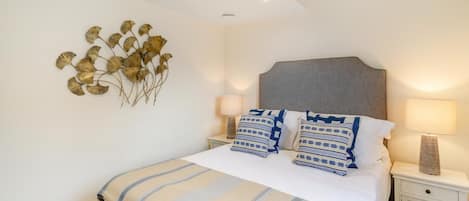 A neatly made bed with striped bedding, two bedside lamps, a decorative wall piece, and a headboard.