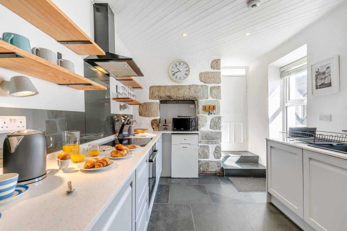 Eine moderne Küche mit Steinwand, integriertem Mikrowellenherd und einer Frühstücksecke mit Croissants und Orangensaft.