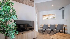 A modern living room with a flat-screen TV, a dining area with a wooden table and four chairs, and a large potted plant. - Modern 2 bedroom apartment in Carrer Balmes (Barcelona)