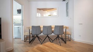 A dining area with a wooden table and three grey chairs, a kitchen with a dishwasher, and a TV in the corner. - Modern 2 bedroom apartment in Carrer Balmes (Barcelona)