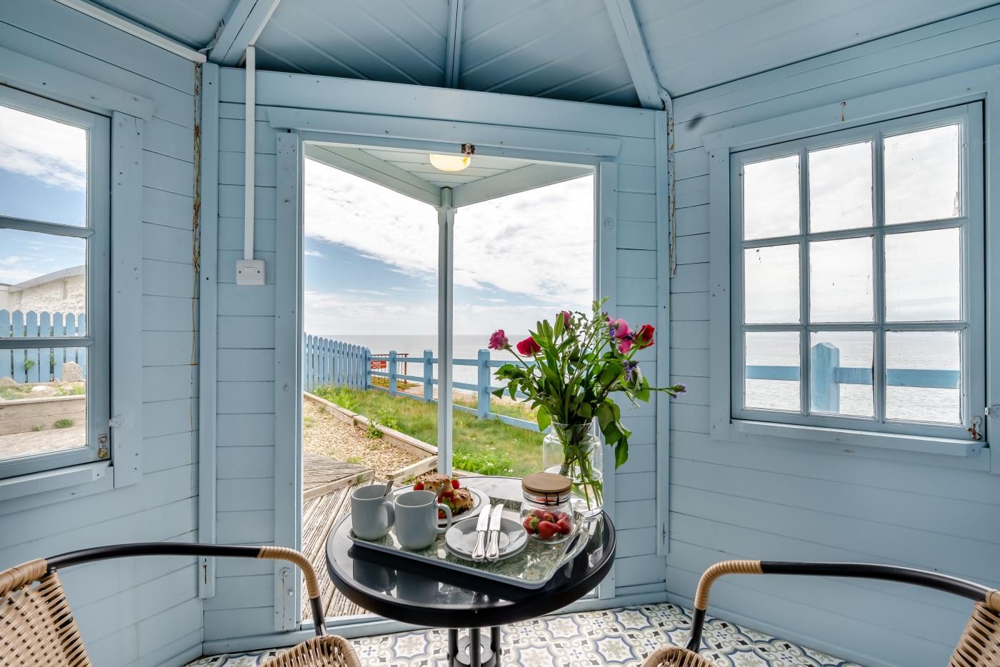 A room with a table set for two, a view of the beach, and a chair.