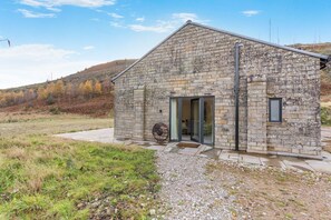 A stone building with a door and a window, surrounded by a gravel path and grassy area.