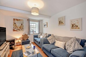 A living room with a sofa, a coffee table, a TV, and artwork on the walls. - 2 Bed in Seahouses (oc-nb1971) (Seahouses)