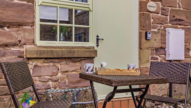 Um edifício de pedra com porta verde, uma janela com um vaso de flores e uma mesa com uma bandeja de pastelaria.