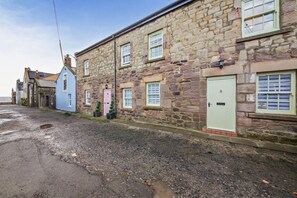 A stone building with multiple windows and doors, a gravel driveway, and a clear sky. - 2 Bed in Seahouses (oc-nb1971) (Seahouses)