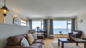 A living room with a leather sofa, a coffee table with fruit, a view of the sea, and a lamp. - 2 Bed in Porthleven (oc-lampho) (Porthleven)