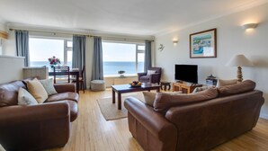A spacious living room with a large window offering a view of the sea, furnished with leather sofas and a flat-screen TV. - 2 Bed in Porthleven (oc-lampho) (Porthleven)