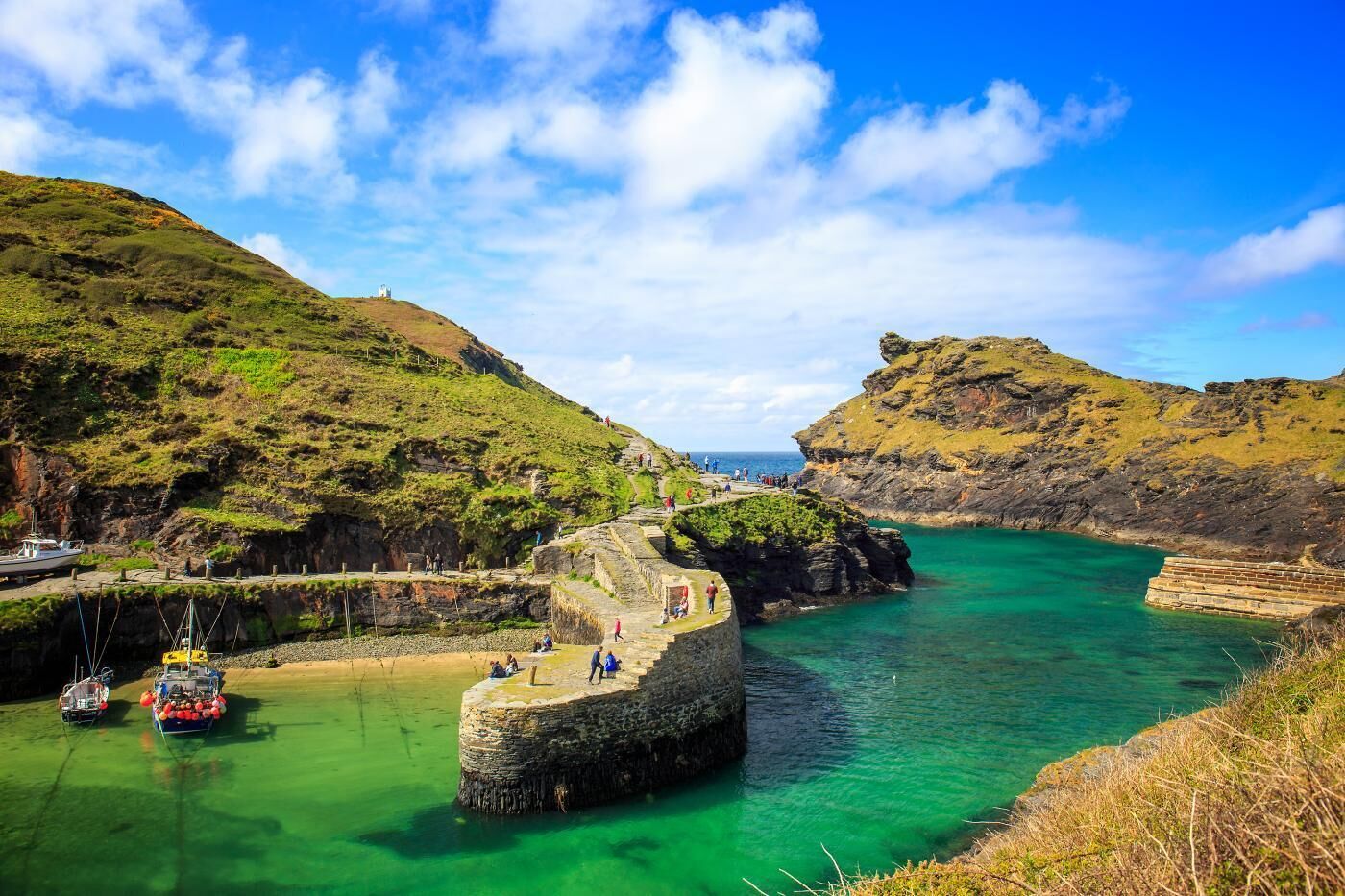 Un paisaje costero con una estructura de piedra, barcos y un mar azul cristalino.