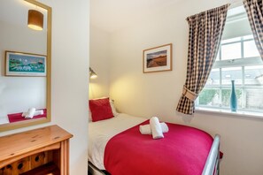 A bedroom with a bed, a bedside table, a mirror, a window with curtains, and two framed pictures. - 2 Bed in Seahouses (oc-nb1972) (Seahouses)