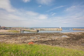 A coastal landscape with a pier extending into the water, a lighthouse, and a rocky shoreline. - 2 Bed in Seahouses (oc-nb1972) (Seahouses)