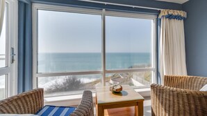 A room with a large window overlooking the ocean, wicker furniture, and a small table with a decorative item. - 3 Bed in Porthleven (oc-oceavi) (Porthleven)