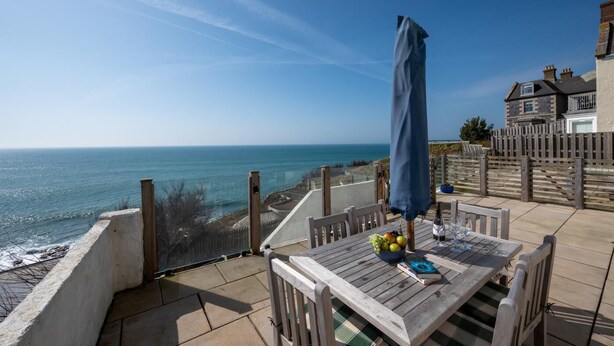 A wooden deck with a table, chairs, and a blue umbrella overlooking the sea. - 3 Bed in Porthleven (oc-oceavi) (Porthleven)