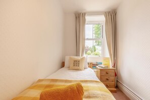Ein Schlafzimmer mit einem Bett, einem Nachttisch, einem Fenster mit Vorhängen und Blick auf Grünlandschaft.