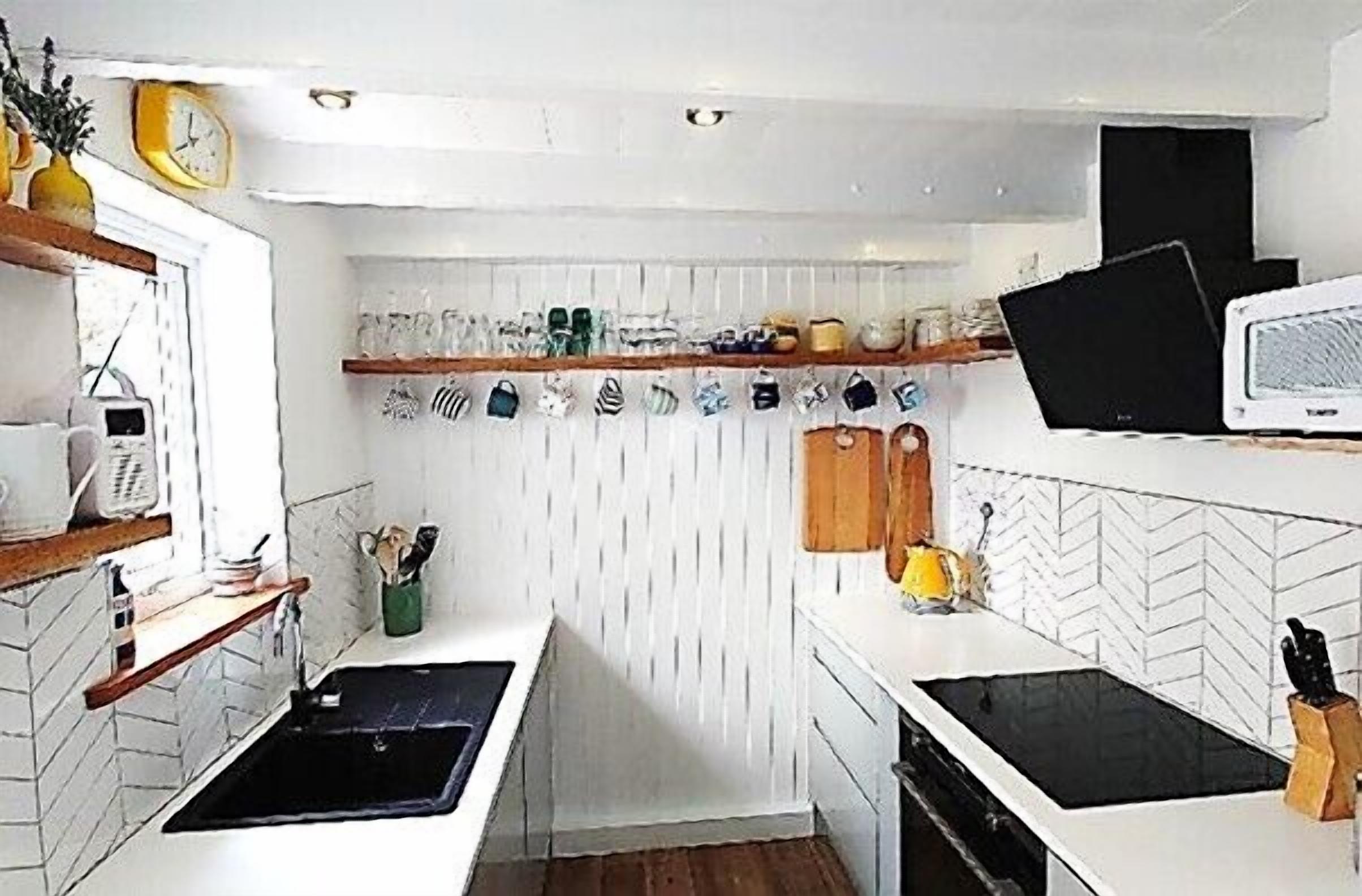 A compact kitchen with white cabinetry, a black sink, a microwave, and a small window.