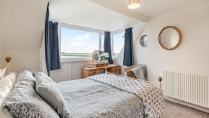 Un dormitorio con cama, cómoda, espejo y vista al exterior.