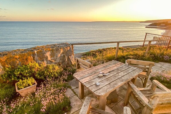 A wooden table and chairs on a stone patio overlooking the sea. - 2 Bed in Porthleven (oc-kelyna) (Porthleven)