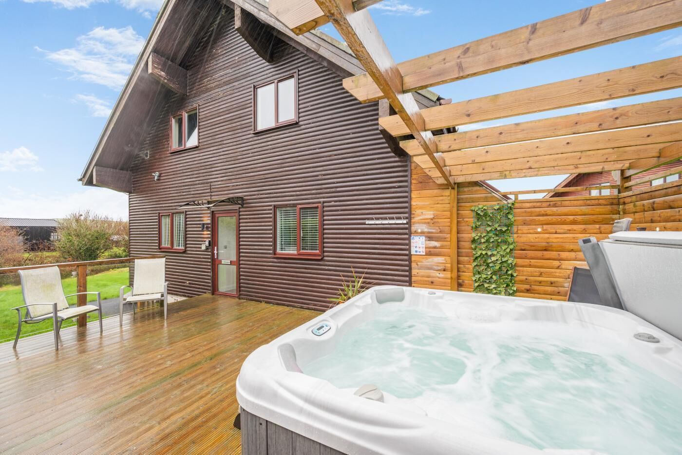Eine Holzhütte mit Whirlpool auf der Terrasse, einer überdachten Veranda und Blick auf die umliegende Landschaft.