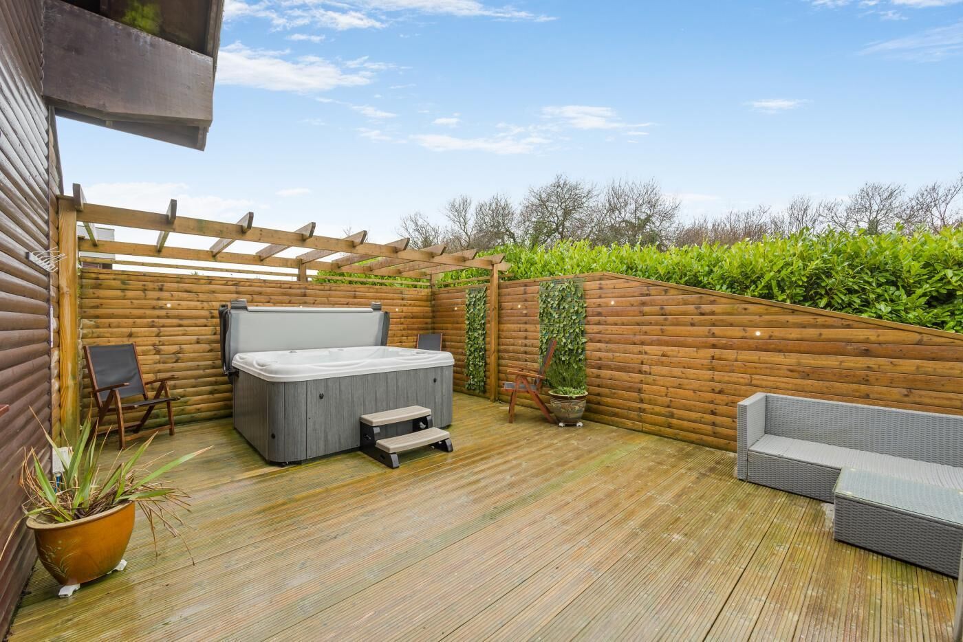 A wooden deck with a hot tub, two chairs, and a small table.
